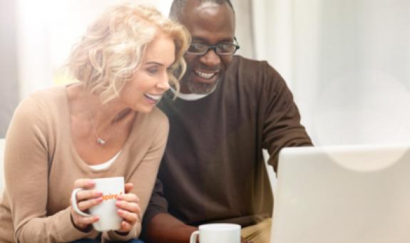 Image of middle aged couple smiling, drinking coffee and looking at their computer