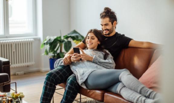 Image of a young couple inside a warm home looking at a smartphone