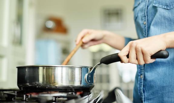 Image of a hand stirring a pot on a natural gas stove
