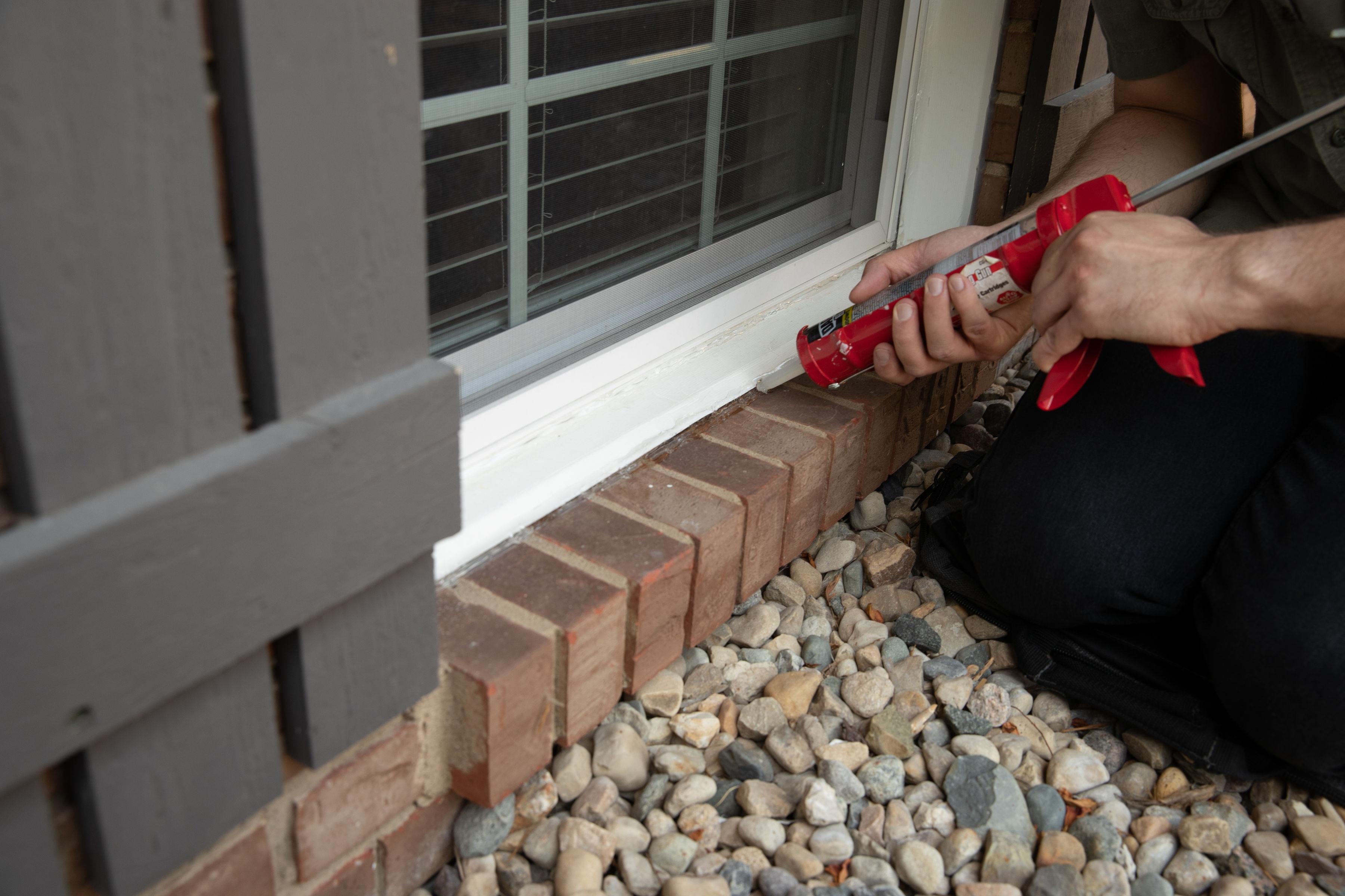 man sealing window on outside of home