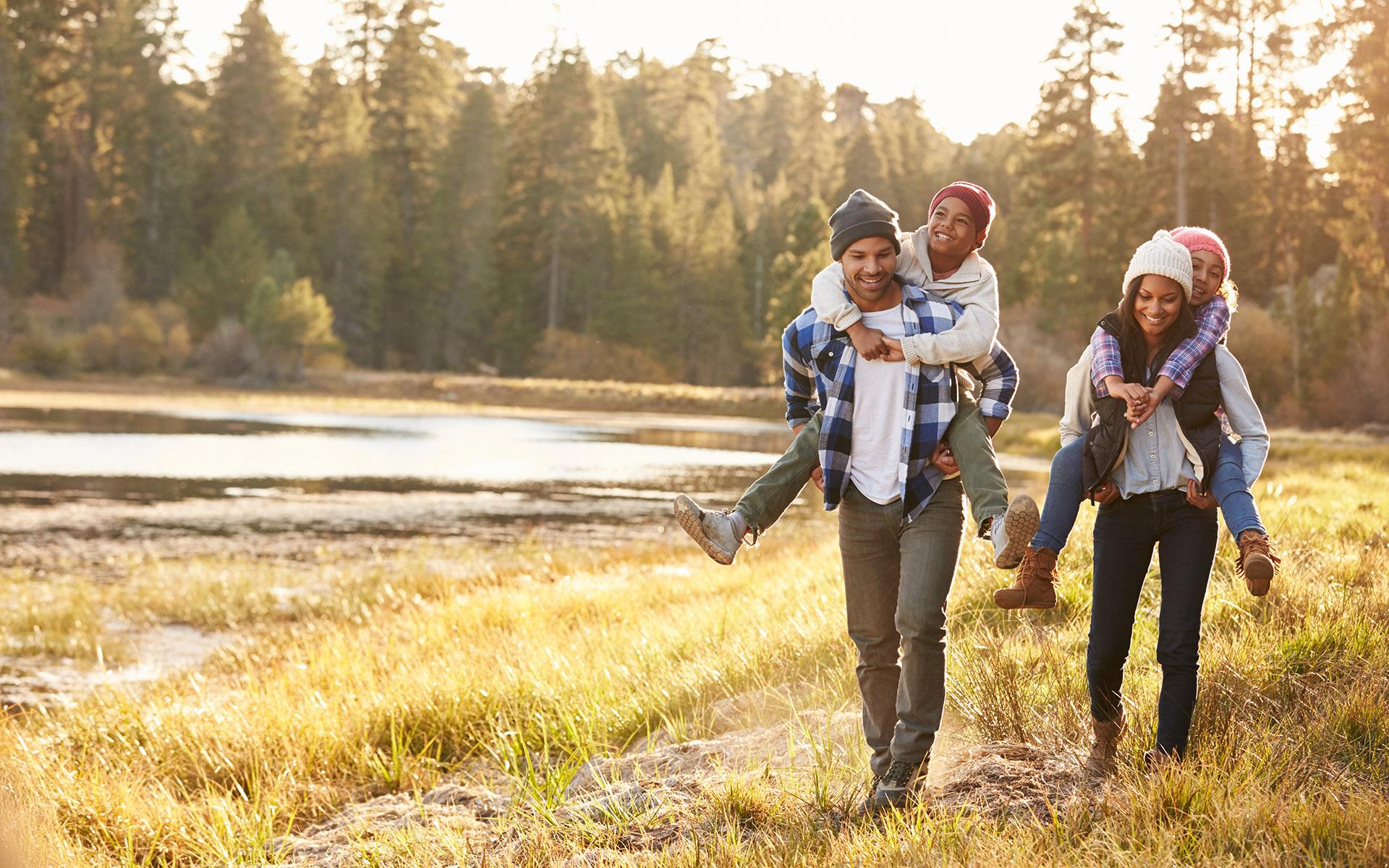 Man and woman with children on backs walking in a field with a stream behind them