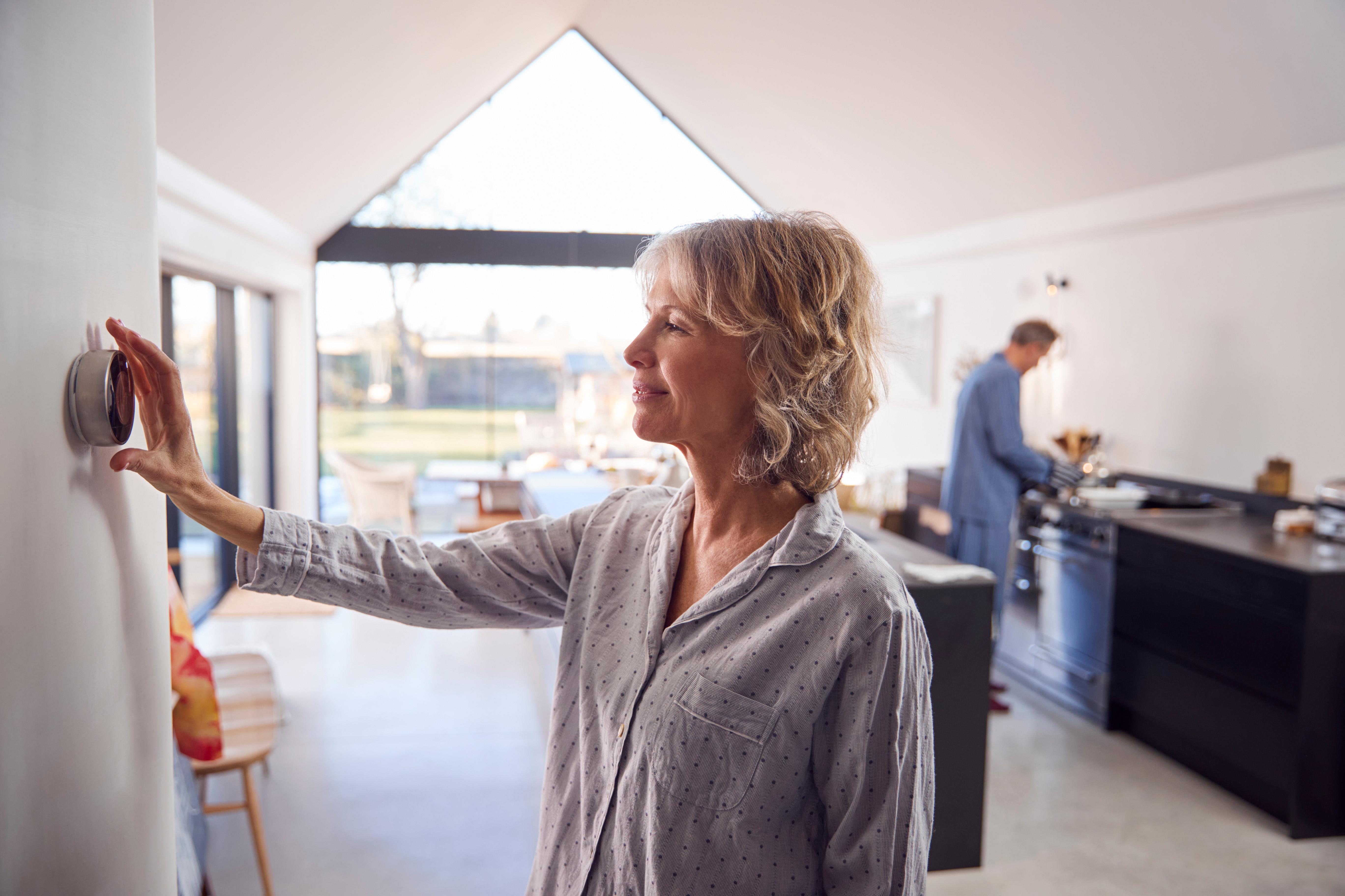 Image of woman adjusting smart thermostat inside her home