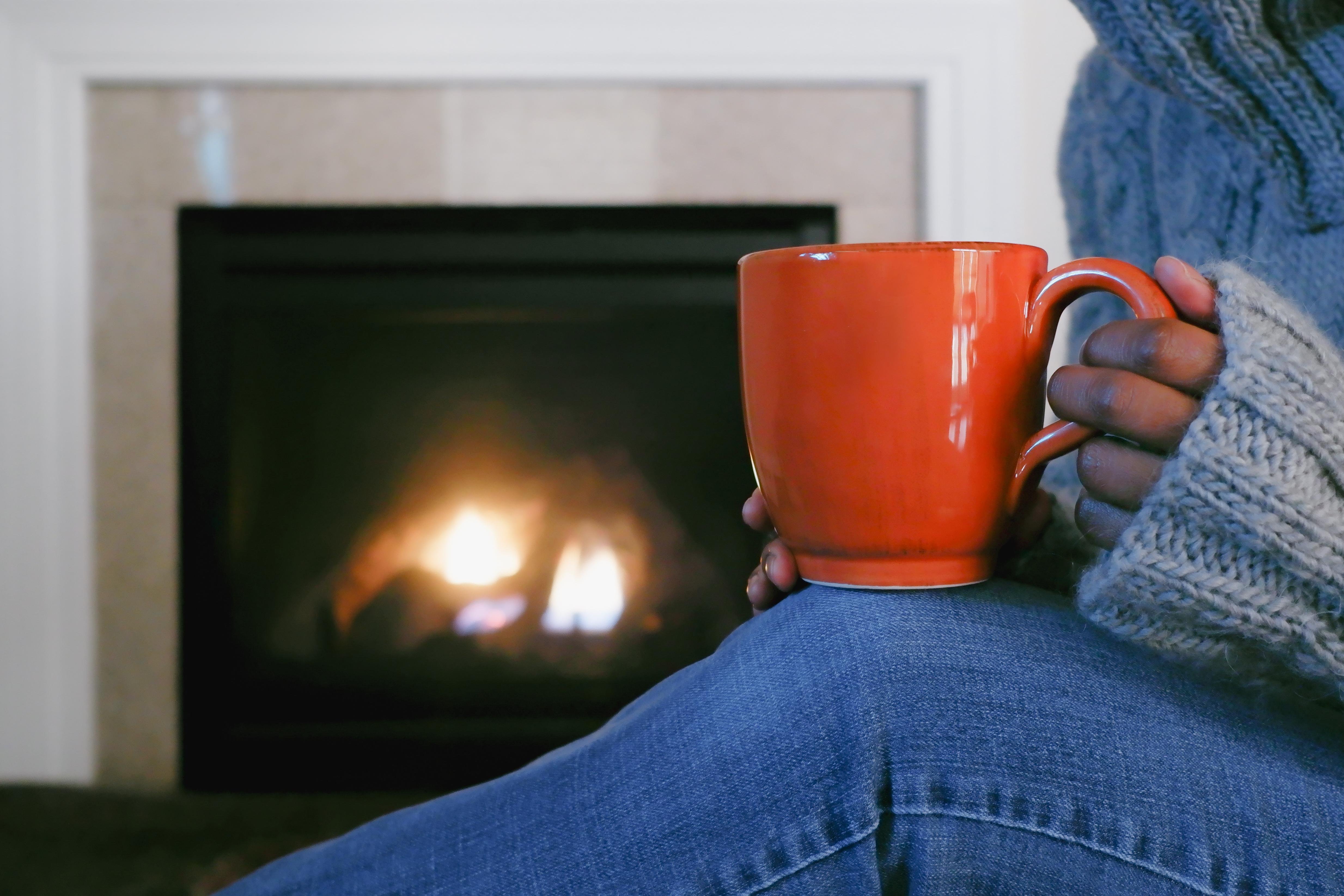 Image of woman sitting in front of fireplace holding an orange mug